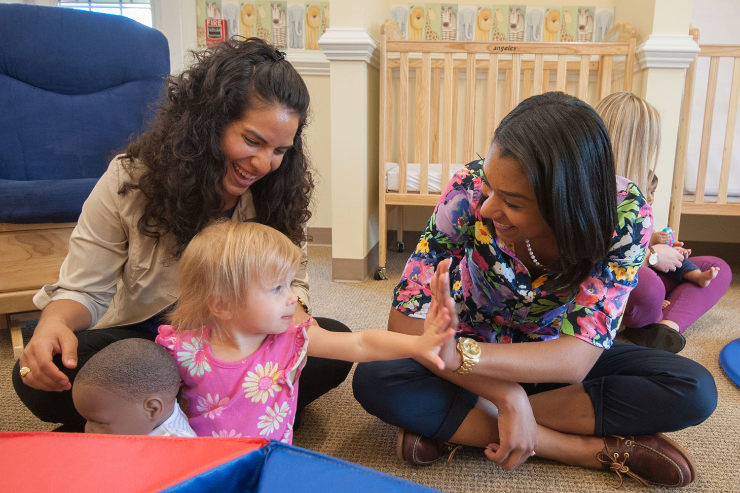 two women sitting in an nursery with a child holding a doll